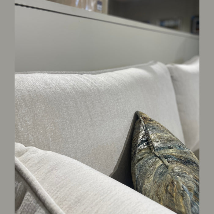 Close-up of the Savoy sofa by vendor-unknown, upholstered in light Aquaclean fabric. Includes a decorative cushion in green, blue, and gold. Soft lighting and neutral décor complete the stylish Irish-made setting.