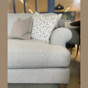 A light gray Monroe Sofa featuring Irish fabric band detailing and two patterned throw pillows, set indoors with a blue partition and tables visible in the background.