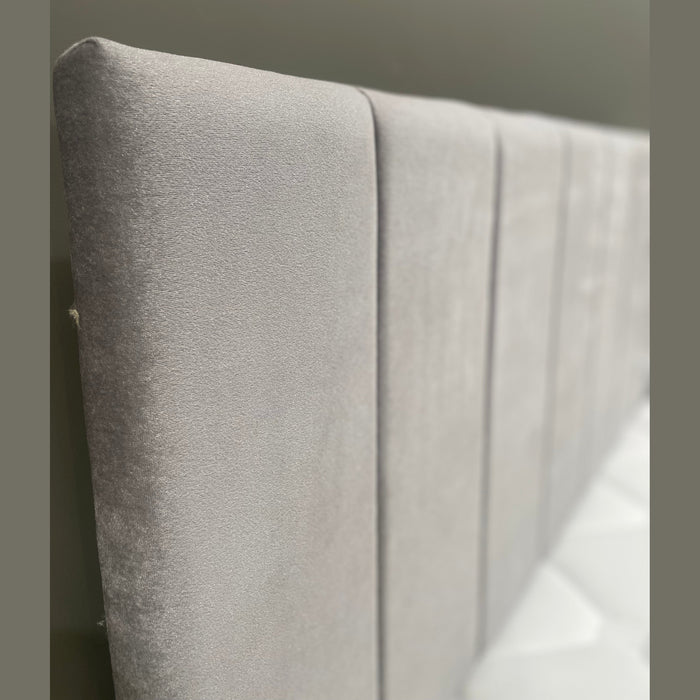 Close-up of a modern gray velvet upholstered headboard with vertical channel stitching.