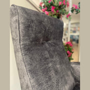 Close-up of the Kelvin Chair, featuring a textured gray fabric and high backrest in an indoor setting. Blurred pink flowers and green leaves in the background add color and softness to this modern chair scene.
