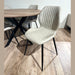 The Elson Round Table with 4 Lyra Chairs features modern dining chairs with light beige, vertically-stitched upholstery and black metal legs, arranged around a round table on a light brown wooden floor.