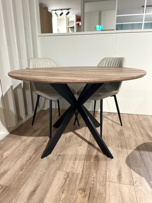 The Elson Round Table with four Lyra Chairs features black X legs and light gray padded seats, creating a modern, minimalistic dining setup on a light wood floor.