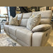 The Jude Recliner is a light gray sofa with washable microfiber fabric, including two patterned pillows and displayed in a modern showroom.