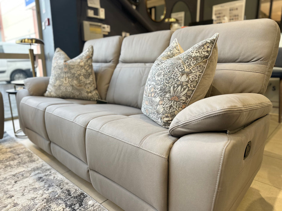 The Jude Recliner is a light gray sofa with washable microfiber fabric, including two patterned pillows and displayed in a modern showroom.