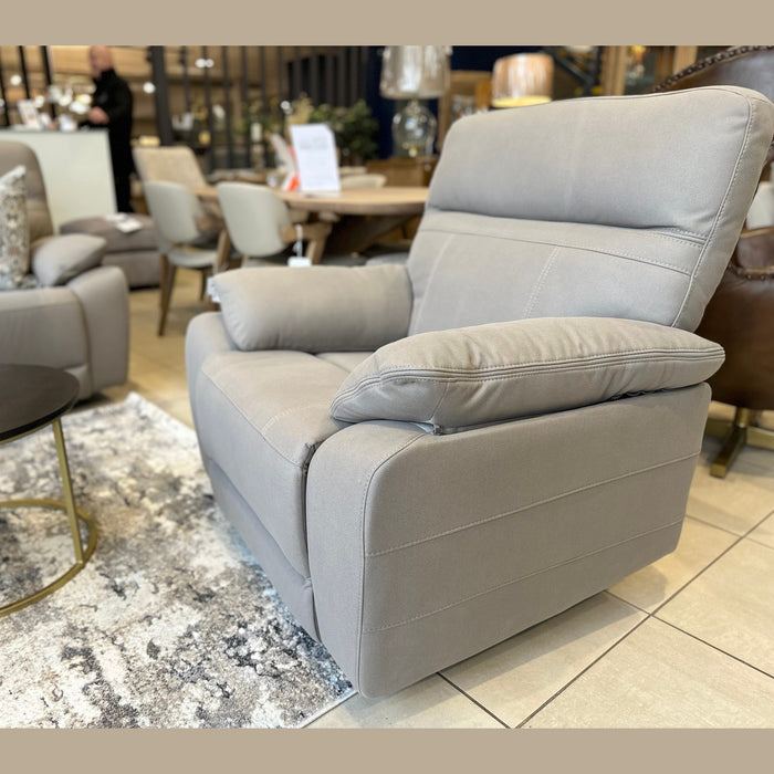 The Jude Recliner, featuring a modern design and light gray washable microfiber, is displayed on a patterned area rug in a showroom with other chairs, tables, and décor.