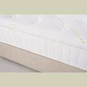 Close-up of the King Koil - Spinal Pocket Pillow Top mattress, featuring a textured, quilted white surface with yellow stitching, set on a beige bed base.