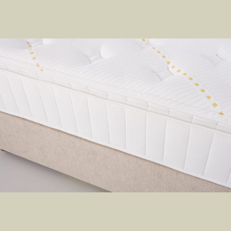 Close-up of the King Koil - Spinal Pocket Pillow Top mattress, featuring a textured, quilted white surface with yellow stitching, set on a beige bed base.