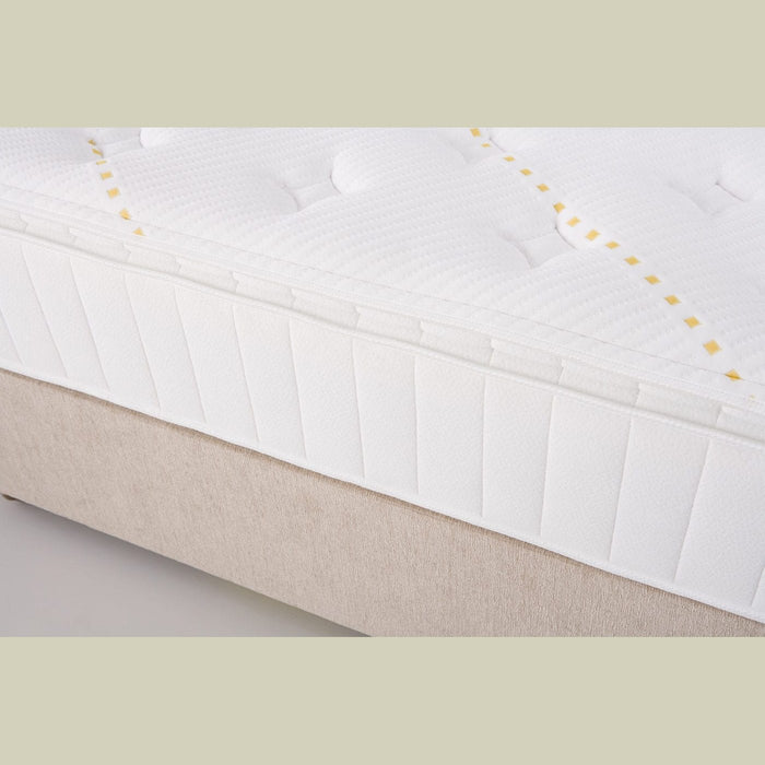 Close-up of the King Koil - Spinal Pocket Pillow Top mattress, featuring a textured, quilted white surface with yellow stitching, set on a beige bed base.