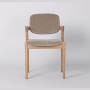 The Mila Dining Chair, crafted from solid wood, features a beige upholstered seat and backrest. Displayed against a plain white background, this chair showcases a simple, modern design with clean lines and no visible armrests.