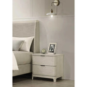 A beige bedside locker placed next to a bed, featuring two drawers and a handle, with a wall lamp above it.