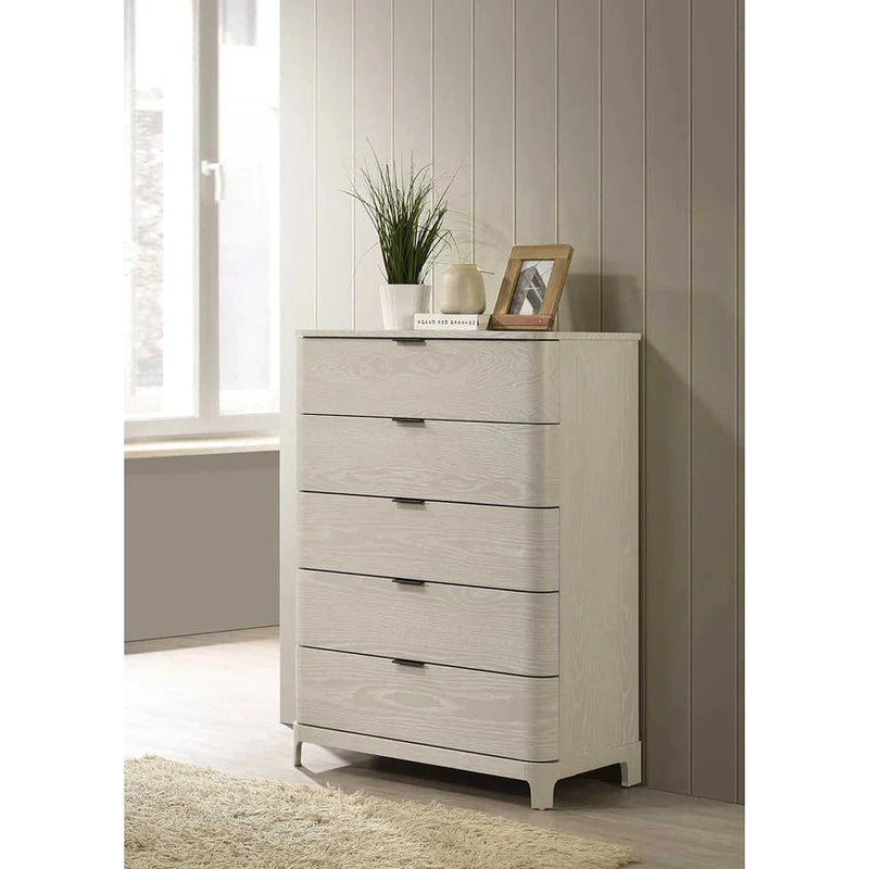 A tall chest of drawers from the Parma Range furniture collection, finished in light ash wood. It has multiple drawers with handles, placed in a room with a window and decorative items on top.