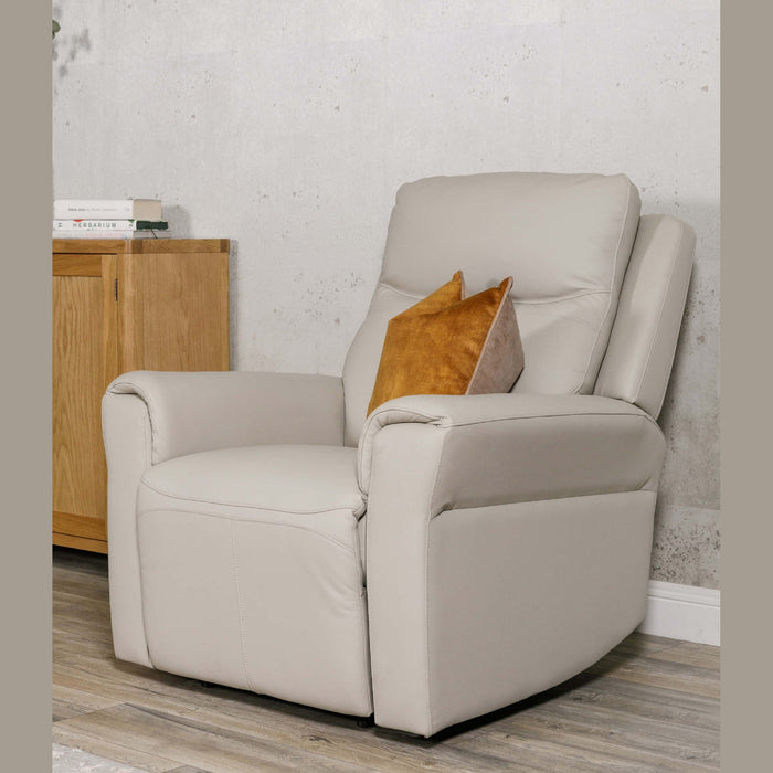 The Russo Electric Recliner - Leather, in light beige with a brown cushion, sits on a wood floor near a wooden cabinet against a light gray wall. Books rest atop the cabinet, and the chair includes a handy USB charging port.