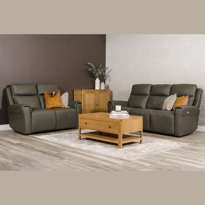 A modern living room with two dark gray leather sofas, including the Russo Electric Recliner - Leather, decorated with throw pillows, a wooden coffee table with books and a candle, a wooden cabinet with vases and greenery, and a light rug on wood flooring.
