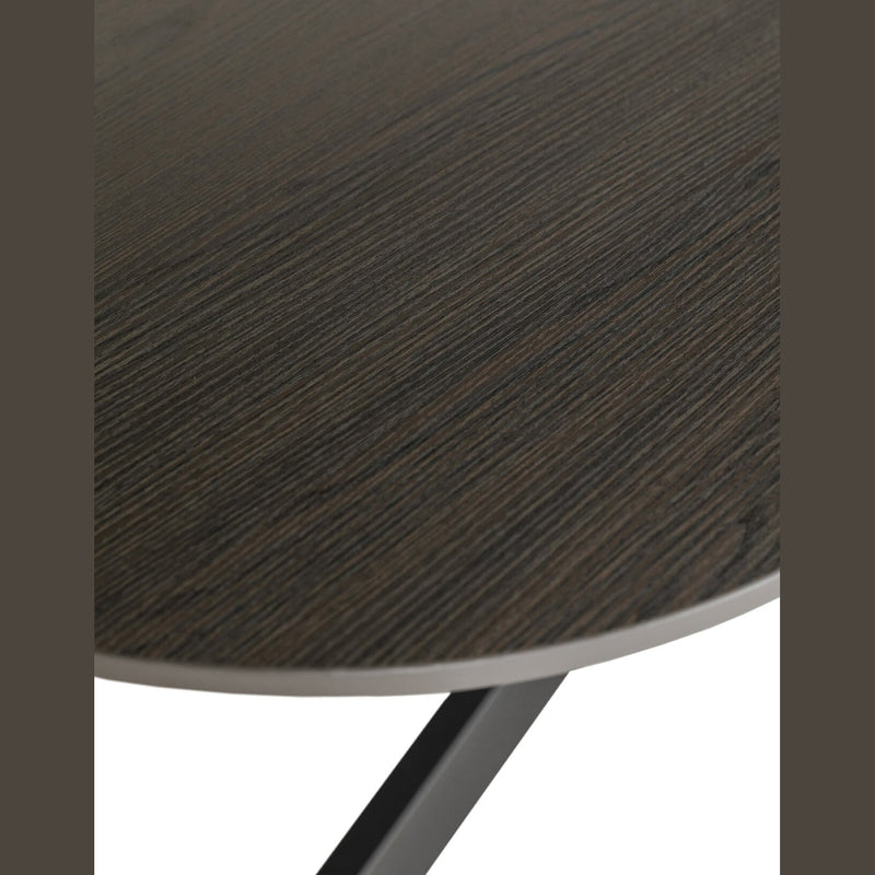 Close-up of the Sadie Oval Dining Table's round tabletop with a dark wood grain finish, highlighting the corner edge and part of its black metal leg underneath.