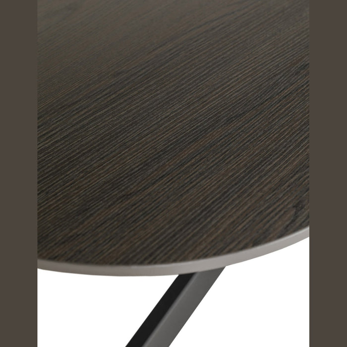 Close-up of the Sadie Oval Dining Table's round tabletop with a dark wood grain finish, highlighting the corner edge and part of its black metal leg underneath.