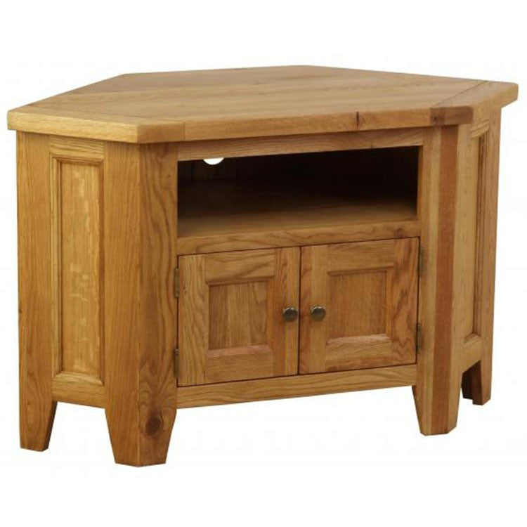 The Saoirse Corner TV Unit is a handmade solid oak stand with a pentagonal top, open shelf, and two cabinet doors with metal knobs. It features simple panel detailing and a light wood finish.