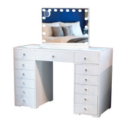 The Erika Hollywood Dressing Table Bluetooth 120cm features a sleek white design with a large, LED-lit mirror. It includes glass tops and twelve drawers adorned with crystal knobs. In the reflection of the mirror, a blurred bed and blue wall can be seen in the background.