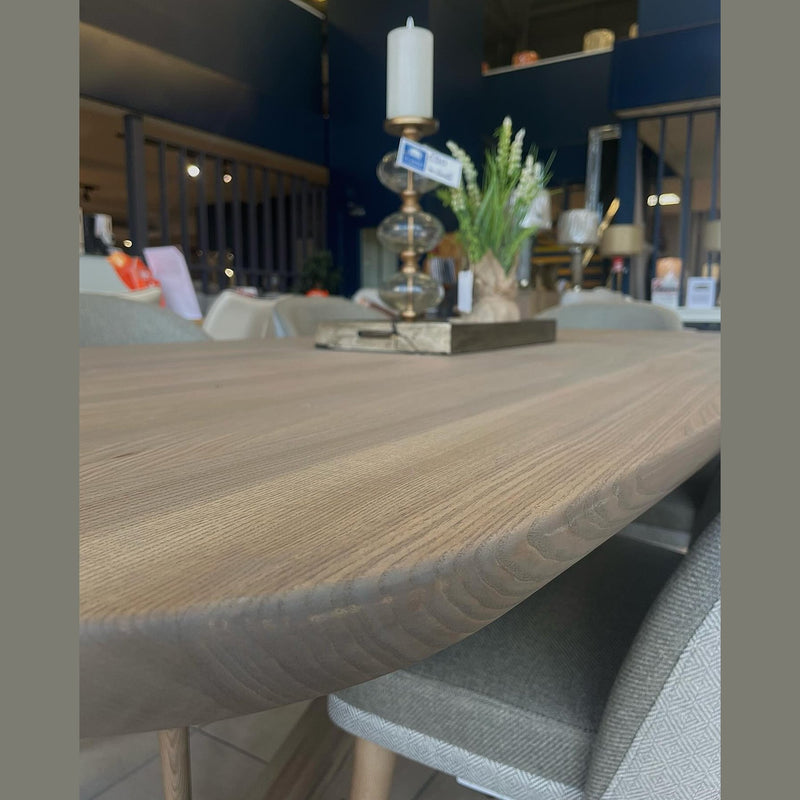 A close-up of the Alcor Dining Table with chairs, featuring a tall candle holder, a small potted plant, and a decorative tray. The modern, well-lit interior is visible in the background.