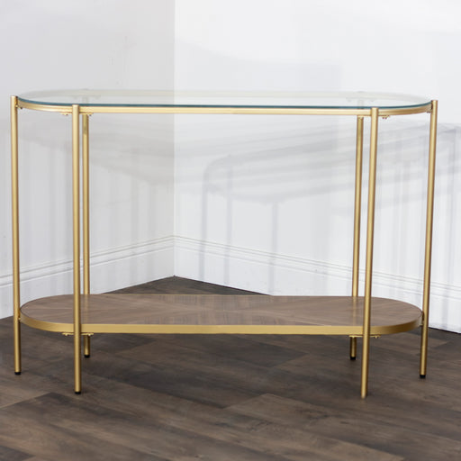The Andrea Console Table showcases elegant style with a gold metal frame, glass top, and wooden lower shelf, perfectly set against a white wall on dark wood flooring.