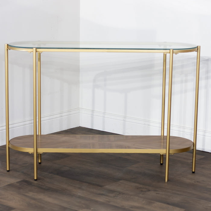 The Andrea Console Table showcases elegant style with a gold metal frame, glass top, and wooden lower shelf, perfectly set against a white wall on dark wood flooring.