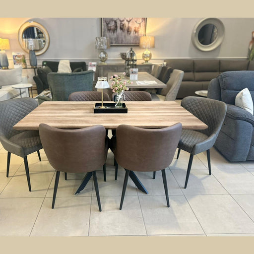The Elson Table & 6 Diamond Chairs - Special Offer features four gray fabric and two brown leather chairs, elegantly displayed in a showroom with sofas, mirrors, lamps, and décor in the background.