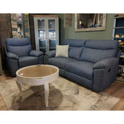 A cozy living room setup with the Vera Recliner Sofa in blue, paired with a matching armchair, a white round coffee table, beige rug, glass-front cabinet, decorative pillow, and wall mirror for a stylish finish.