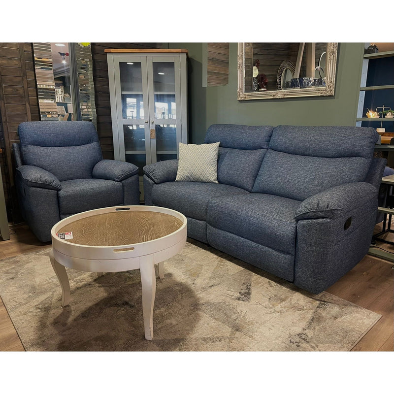 A cozy living room setup with the Vera Recliner Sofa in blue, paired with a matching armchair, a white round coffee table, beige rug, glass-front cabinet, decorative pillow, and wall mirror for a stylish finish.