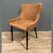 The Diamond Dining Chair, featuring a brown quilted fabric, curved backrest, and black tapered legs, stands on a wooden floor against a plain gray wall.