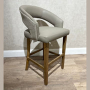 The Willow Counter Stool features a modern counter-height design with a light wood frame, tan cushioned seat, and curved backrest upholstered in smooth and textured beige fabric, shown against a light wall and wood floor.