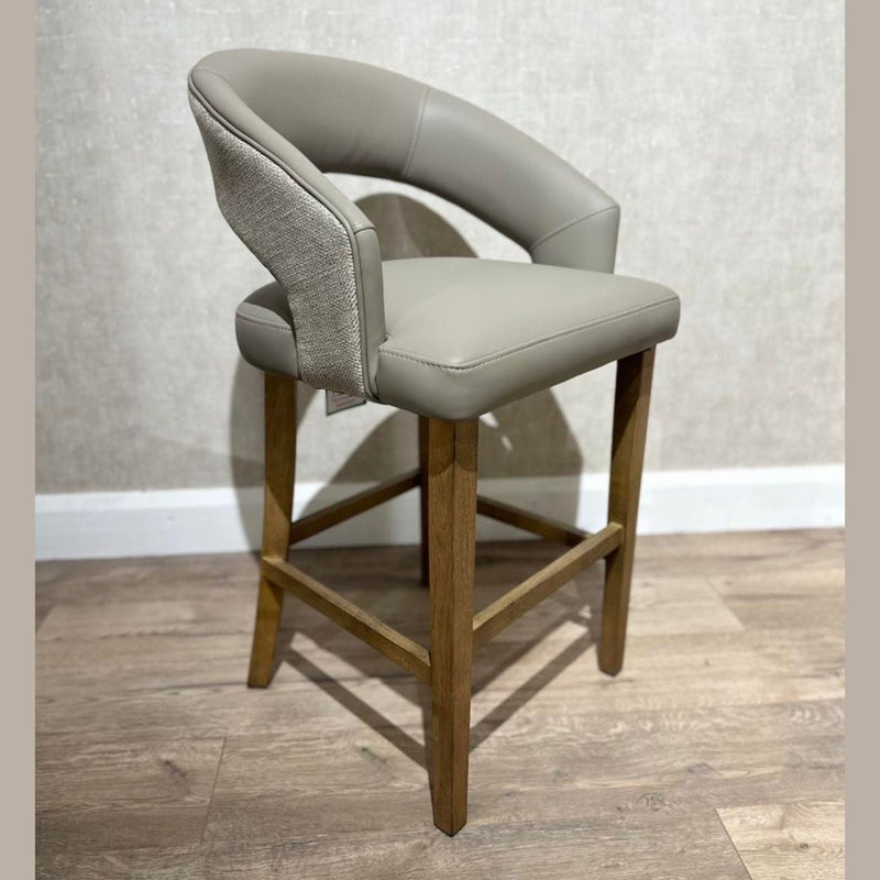 The Willow Counter Stool features a modern counter-height design with a light wood frame, tan cushioned seat, and curved backrest upholstered in smooth and textured beige fabric, shown against a light wall and wood floor.