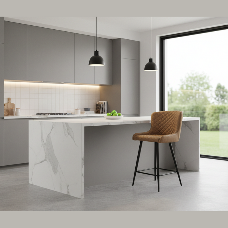 A modern kitchen with gray cabinets, a marble island, and a Diamond Counter Stool with quilted diamond stitching in brown PU leather. Two black pendant lights hang above the island, while large glass doors showcase a lush outdoor view.