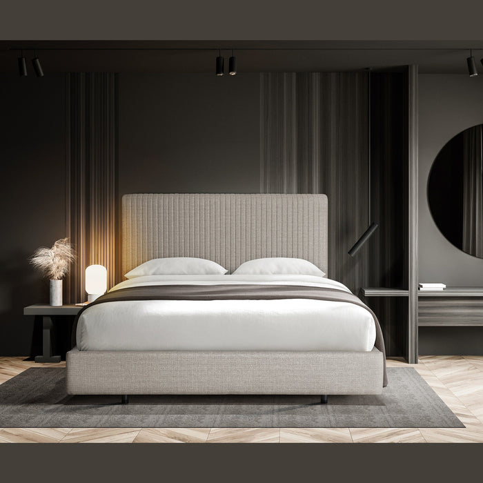 A modern minimalist bedroom featuring the Valerie Bedframe, white bedding, a dark accent wall, round mirror, bedside table with lamp and dried pampas grass, all atop wood flooring in a striking herringbone pattern.