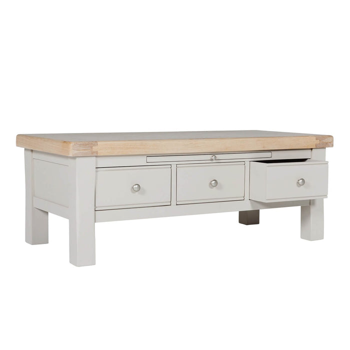 Rectangular table with a natural wood top and a painted gray base featuring three storage drawers, one of which is open.