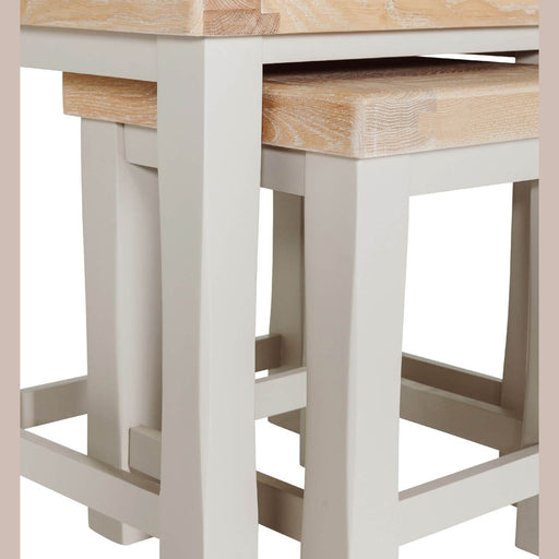 Close-up of a light wood table with matching benches tucked underneath; both feature taupe-painted legs and natural oak tops, echoing the Doune Nest of Tables style.