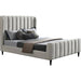The Isobella Bedframe is a modern upholstered bed featuring a high headboard with vertical channel tufting in soft stone linen, styled with grey and black bedding, multiple pillows, and a folded brown blanket at the foot.