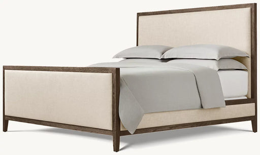The Hampshire Bedframe features a dark wood frame with beige upholstered headboard and footboard, styled with light gray bedding and two stacked pillows, all set against a simple light background.