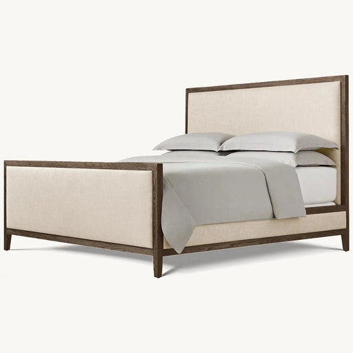 The Hampshire Bedframe features a dark wood frame with beige upholstered headboard and footboard, styled with light gray bedding and two stacked pillows, all set against a simple light background.