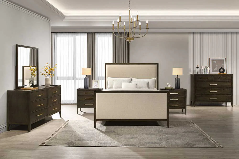 Modern bedroom featuring a Hampshire Bedframe in beige upholstery, two dark wood nightstands, matching dresser and chest, mirror, table lamps, chandelier, floor rug, and large windows with sheer curtains for a serene vibe.