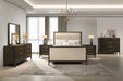 Modern bedroom featuring a Hampshire Bedframe in beige upholstery, two dark wood nightstands, matching dresser and chest, mirror, table lamps, chandelier, floor rug, and large windows with sheer curtains for a serene vibe.