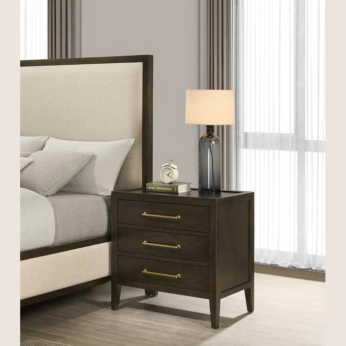 A modern bedroom features a beige upholstered bed beside the Hampshire Locker, a dark wooden nightstand with gold handles, topped with a gray lamp, a book, and a small décor piece. Light filters in through sheer curtains.