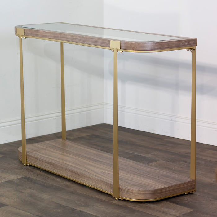 The Hannah Console Table features a wood finish, glass top, modern gold legs, and a wood-finish lower shelf. Rounded corners add to its sleek design, making it stand out against white walls and dark wood floors.