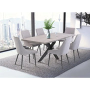 A modern dining room features a Rimini Dining Table in stone melamine, six light gray chairs, a vase with green fern leaves, and a gray rug. Large windows frame a stunning city skyline in the background.