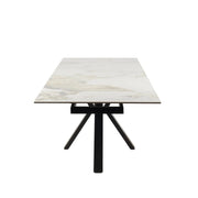 The Sorrento Dining Table features a modern design with a light marble-style top and black metal legs arranged in a central, angled base, shown from the short end facing the viewer.