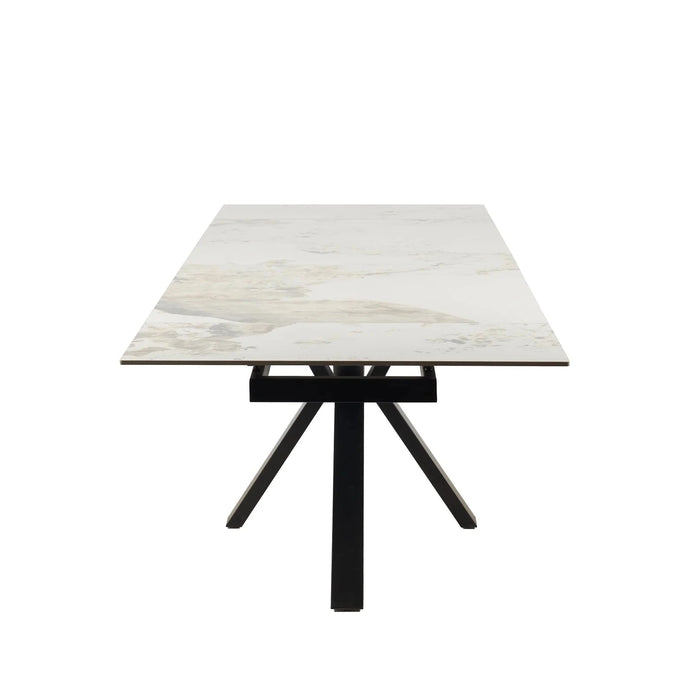 The Sorrento Dining Table features a modern design with a light marble-style top and black metal legs arranged in a central, angled base, shown from the short end facing the viewer.