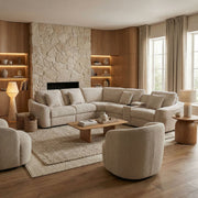 A modern living room featuring the Velora Corner Group, a large beige chenille sectional sofa, paired with round chairs, a stone fireplace, built-in wood shelves, a wooden coffee table, neutral decor accents, and expansive windows dressed with light curtains.