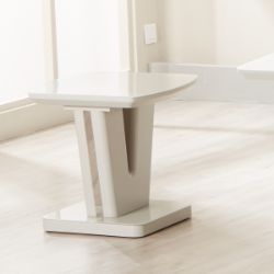 The Vicenza Lamp Table, featuring a modern white finish and unique geometric design, is showcased on a light wood floor in a bright room with large windows.