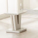 The Vicenza Lamp Table, featuring a modern white finish and unique geometric design, is showcased on a light wood floor in a bright room with large windows.